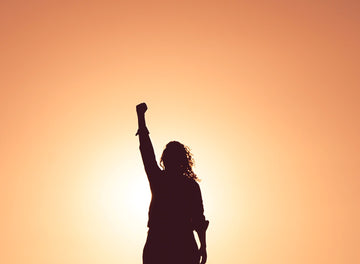 A woman holds up a fist in front of the sunset. 